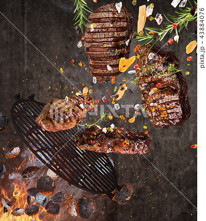 Kettle grill with hot briquettes, cast iron grate and tasty meats flying in the air. 43884076