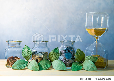 Coin jars with plant and hourglass. Saving money Coin jars with plant and hourglass. Saving money 43889386