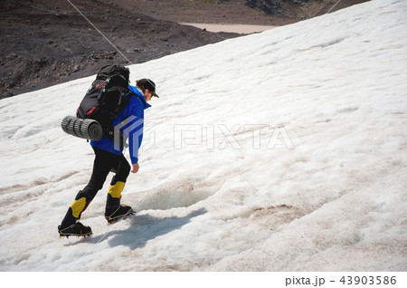 A mountaineer with a backpack walks in crampons walking along a dusty glacier with sidewalks in the 43903586