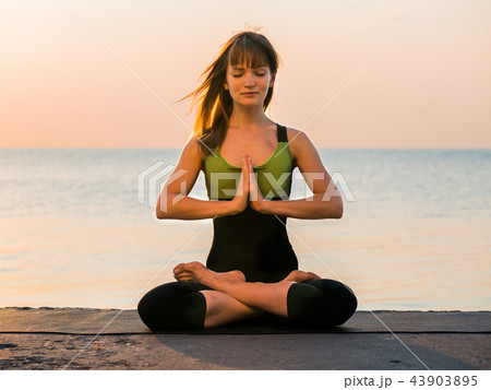 Young caucasian woman in bodysuit relaxing by practicing yoga on the beach near calm sea, close-up 43903895