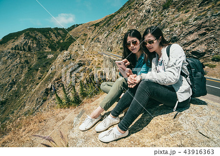girls checking the phone while sitting on cliff 43916363