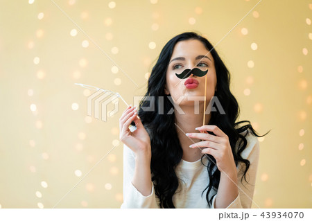 Young woman holding a paper mustache party stick Young woman holding a paper mustache party stick 43934070