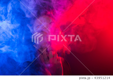 Young woman smoking vape or e-cigarette in neon light Young woman smoking vape or e-cigarette in neon light 43951214
