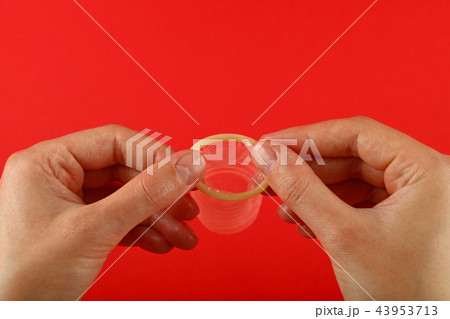 Close up woman hands holding open condom over red Close up woman hands holding open condom over red 43953713