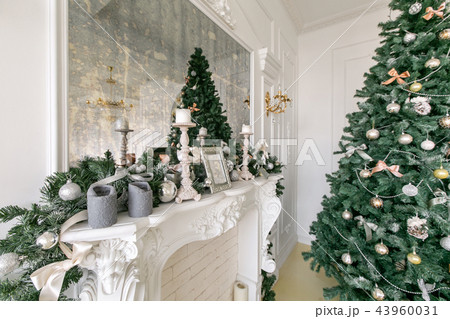 White fireplace decorated with candles and fir branches. Decorated Christmas tree. Classic White fireplace decorated with candles and fir branches. Decorated Christmas tree. Classic 43960031
