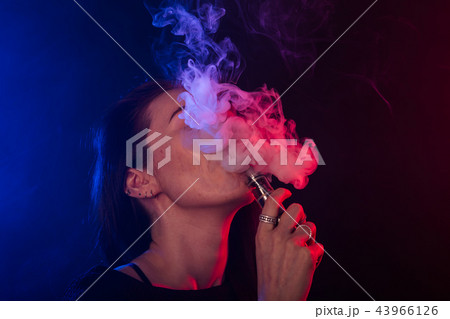 Portrait of young woman in neon red and blue smoke with vape or e-cigarettes Portrait of young woman in neon red and blue smoke with vape or e-cigarettes 43966126