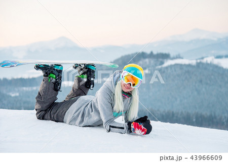 Young woman snowboarder relaxing outdoors lying on the snow smiling to the camera joyfully 43966609