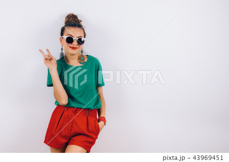 beautiful woman in sunglasses wearing in red shorts and green T-shirt standing near white wall 43969451