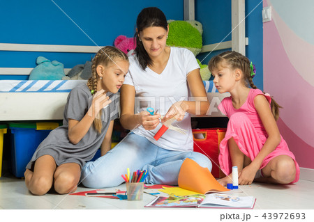 Mom shows daughters how to cut out figures 43972693