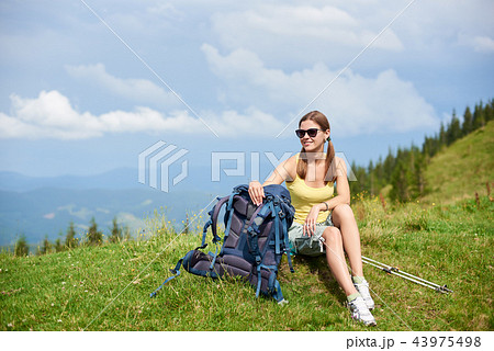 Woman hiker hiking on grassy hill, wearing backpack, using trekking sticks in the mountains 43975498