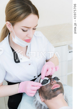 The cosmetologist in pink gloves with a brush applies a carbon mask for peeling on the face of a 43975706