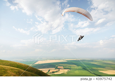 A white-orange paraglider flies over the mountainous terrain A white-orange paraglider flies over the mountainous terrain 43975742