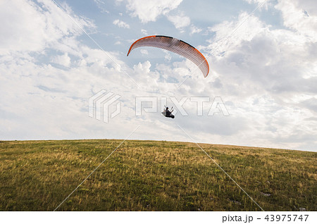 A white-orange paraglider flies over the mountainous terrain A white-orange paraglider flies over the mountainous terrain 43975747