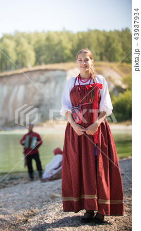 Portreat of a young woman in a Russian folk costume stands on the background of a wonderful 43987934