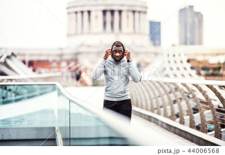 Black man runner with smartphone in an armband on the bridge in a city, resting. 44006568