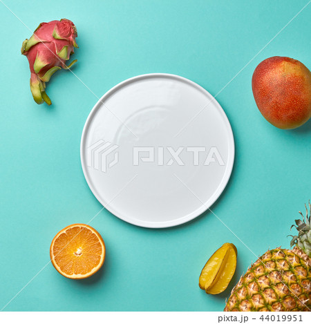 Different tropical fruits and empty white plate on a blue background with copy space. Flat lay 44019951