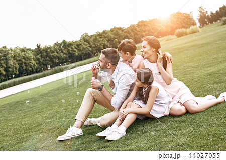 Bonding. Family of four sitting on a grassy field blowing bubble 44027055
