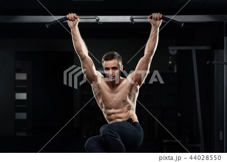 Muscular male athlete pulling up on horizontal bar in dark gym. Muscular male athlete pulling up on horizontal bar in dark gym. 44028550