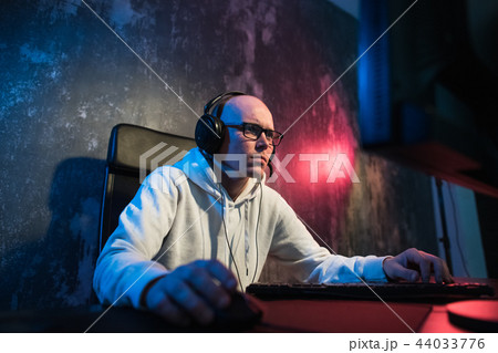 Portrait of concentrated young man in glasses and headset in dark room playing online computer game Portrait of concentrated young man in glasses and headset in dark room playing online computer game 44033776