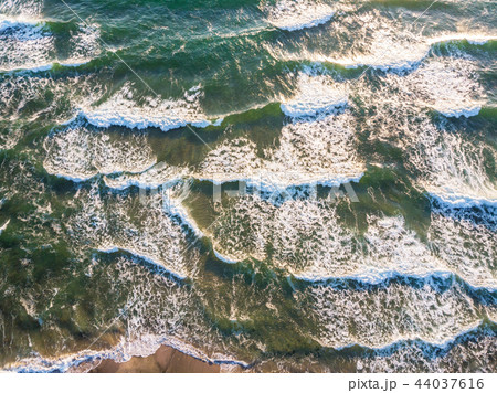 Aerial view of ocean waves crashing on beach. 44037616
