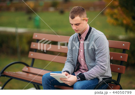 A cute student sits on the bench and writes down his thoughts in his notebool using a pensil. study 44050799