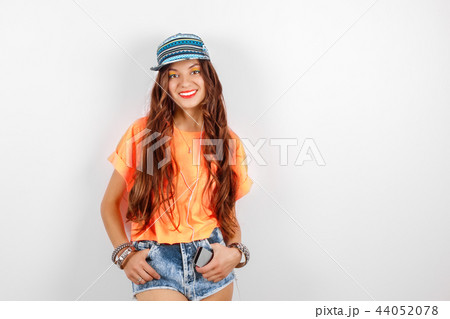 Young smiling hipster woman wearing in blue cap and orange T-shirt listening music in headphones 44052078