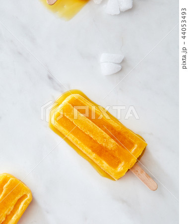 Orange melting ice cream lolly with ice slices on a gray marble table with a copy of the space. Flat Orange melting ice cream lolly with ice slices on a gray marble table with a copy of the space. Flat 44053493