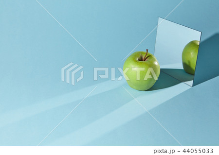 The apple is green, a square mirror on a blue background, a reflection of an apple and from shadows 44055033