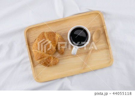 A cup of coffee and croissant on white bed  44055118