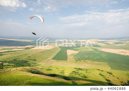 A white-orange paraglider flies over the mountainous terrain A white-orange paraglider flies over the mountainous terrain 44062886