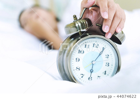 Sleepy woman in bed extending hand to alarm clock 44074622