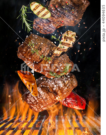 Tasty beef steaks flying above cast iron grate with fire flames. 44094635