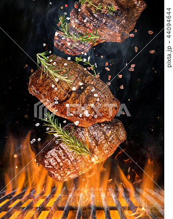 Tasty beef steaks flying above cast iron grate with fire flames. Tasty beef steaks flying above cast iron grate with fire flames. 44094644