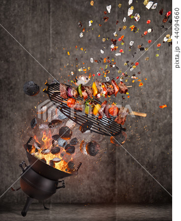 Kettle grill with hot briquettes, cast iron grate and tasty skewers flying in the air. 44094660