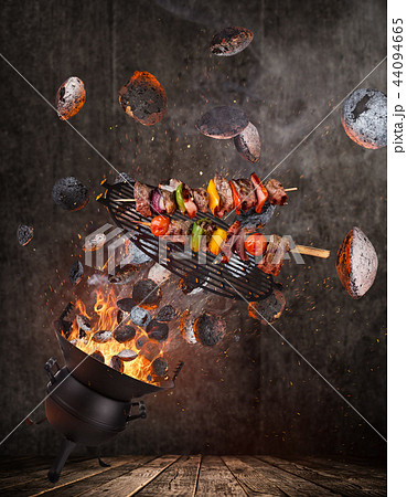 Kettle grill with hot briquettes, cast iron grate and tasty skewers flying in the air. 44094665