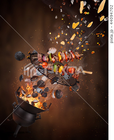 Kettle grill with hot briquettes, cast iron grate and tasty skewers flying in the air. 44094702