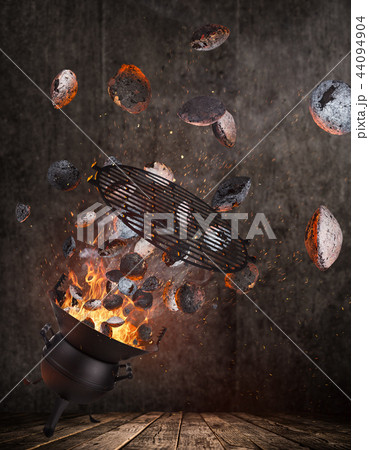 Kettle grill with hot briquettes and cost iron grid flying in the air. 44094904
