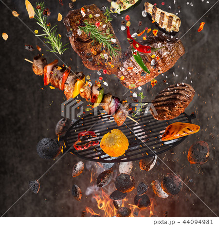 Kettle grill with hot briquettes, cast iron grate and tasty meats flying in the air. 44094981