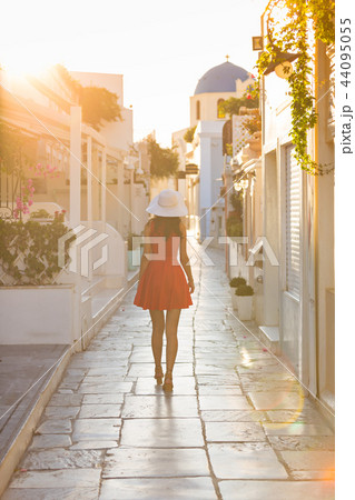 Santorini travel tourist brunette woman in red dress visiting famous white Oia village. Santorini travel tourist brunette woman in red dress visiting famous white Oia village. 44095055