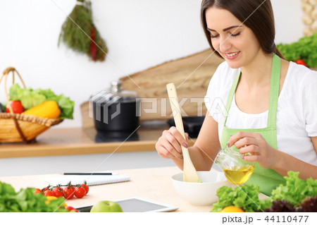 Beautiful Hispanic woman cooking in kitchen while using tablet computer and wooden spoon. Housewife Beautiful Hispanic woman cooking in kitchen while using tablet computer and wooden spoon. Housewife 44110477