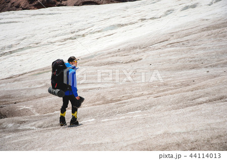 A mountaineer with a backpack walks in wheelchairs, stands on a dusty glacier with sneakers in the A mountaineer with a backpack walks in wheelchairs, stands on a dusty glacier with sneakers in the 44114013
