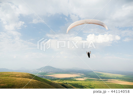 A white-orange paraglider flies over the mountainous terrain A white-orange paraglider flies over the mountainous terrain 44114058