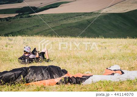 A professional paraglider in full gear and a helmet lies and rests on the grass high in the A professional paraglider in full gear and a helmet lies and rests on the grass high in the 44114070