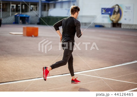 male athlete wearing black sportwear running at track, side view 44126465