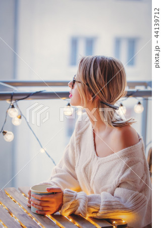 Young woman with cup of coffee near fairy lights  44139712