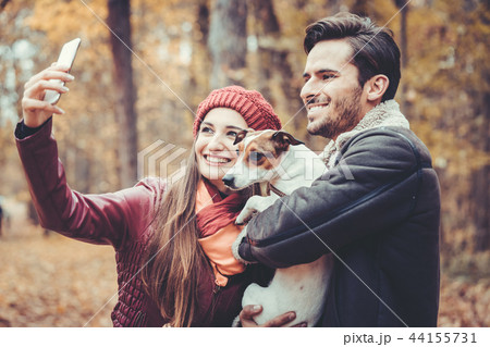 Woman and man with their dog on autumn walk taking a phone selfie 44155731