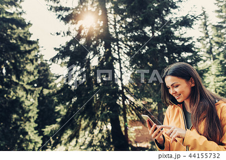 Charming girl using smartphone in sunny coniferous wood Charming girl using smartphone in sunny coniferous wood 44155732