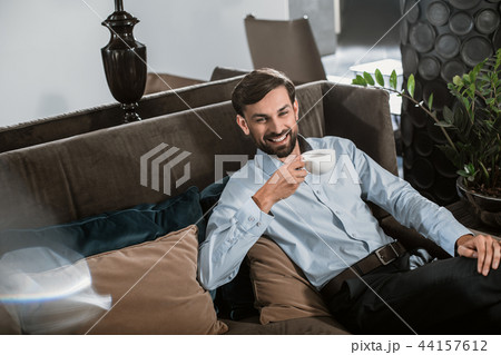 Cheerful businessman is relaxing on couch with hot drink 44157612