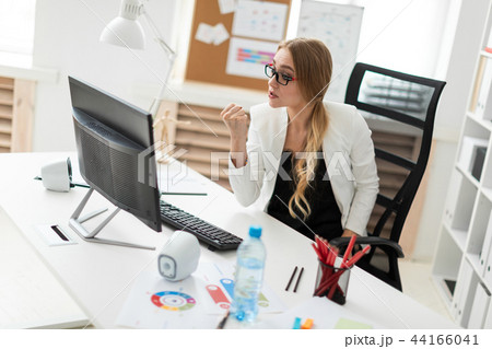 A young girl is sitting at a table in the office, looking at the monitor and showing a fist. 44166041