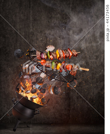 Kettle grill with hot briquettes, cast iron grate and tasty skewers flying in the air. Kettle grill with hot briquettes, cast iron grate and tasty skewers flying in the air. 44173456